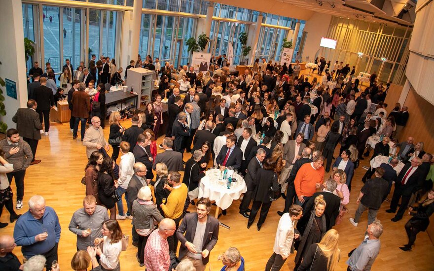 Eine sehr große Gruppe von Personen steht im Foyer der Stadthalle in kleineren Gruppen zusammen und unterhält sich