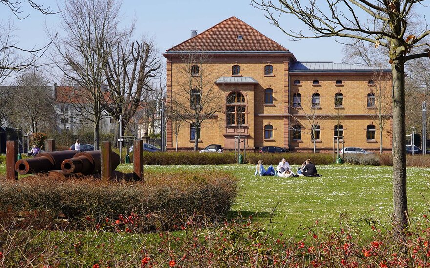 Studierende sitzen vor Gebäude 22 auf der Campuswiese.