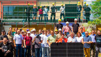 Gruppenfoto bei gutem Wetter vor und auf einem Gebäude einer Grundschule mit Photovoltaik-Anlage, viele Personen tragen Bauhelme