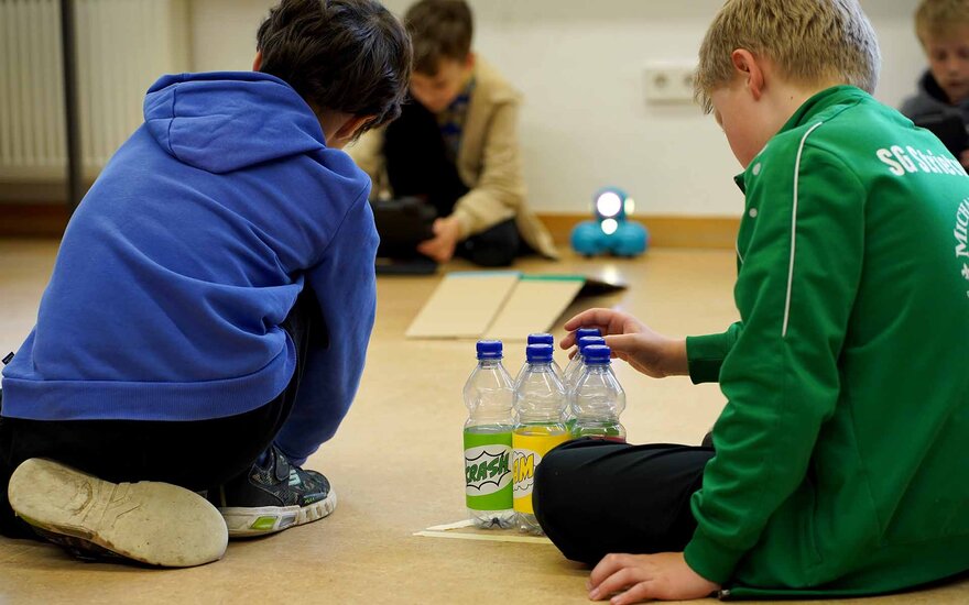 Drei Kinder spielen mit Plastikflaschen auf dem Boden.