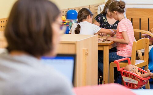 Eltern-Kind-Carell in der Bibliothek, zwei Studentinnen lernen und die Kinder spielen