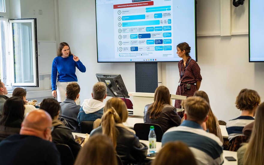 Zwei Professorinnen halten in einem Hörsaal mit zwei Screens einen Vortrag.