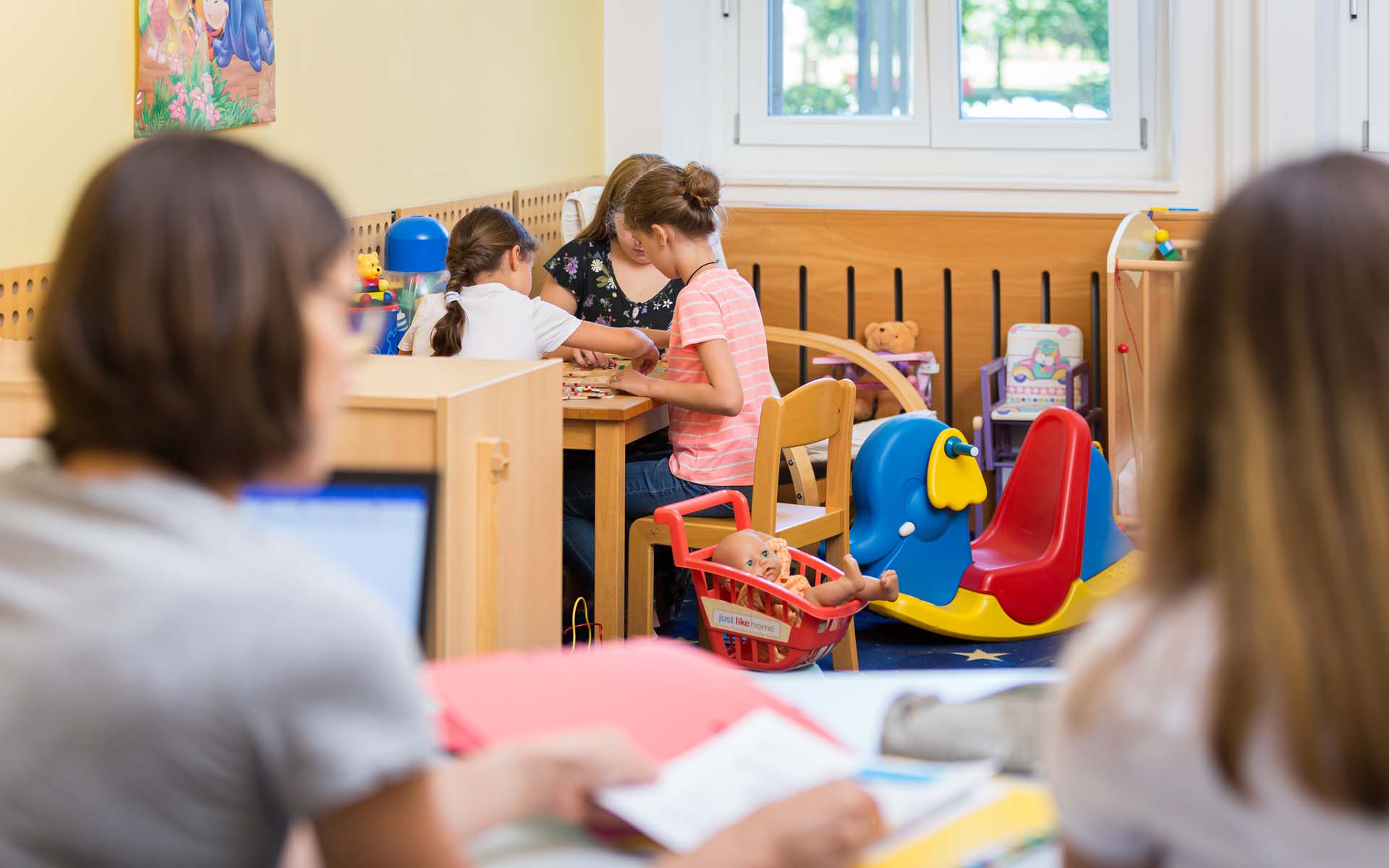 Eltern-Kind-Carell in der Bibliothek, zwei Studentinnen lernen und die Kinder spielen