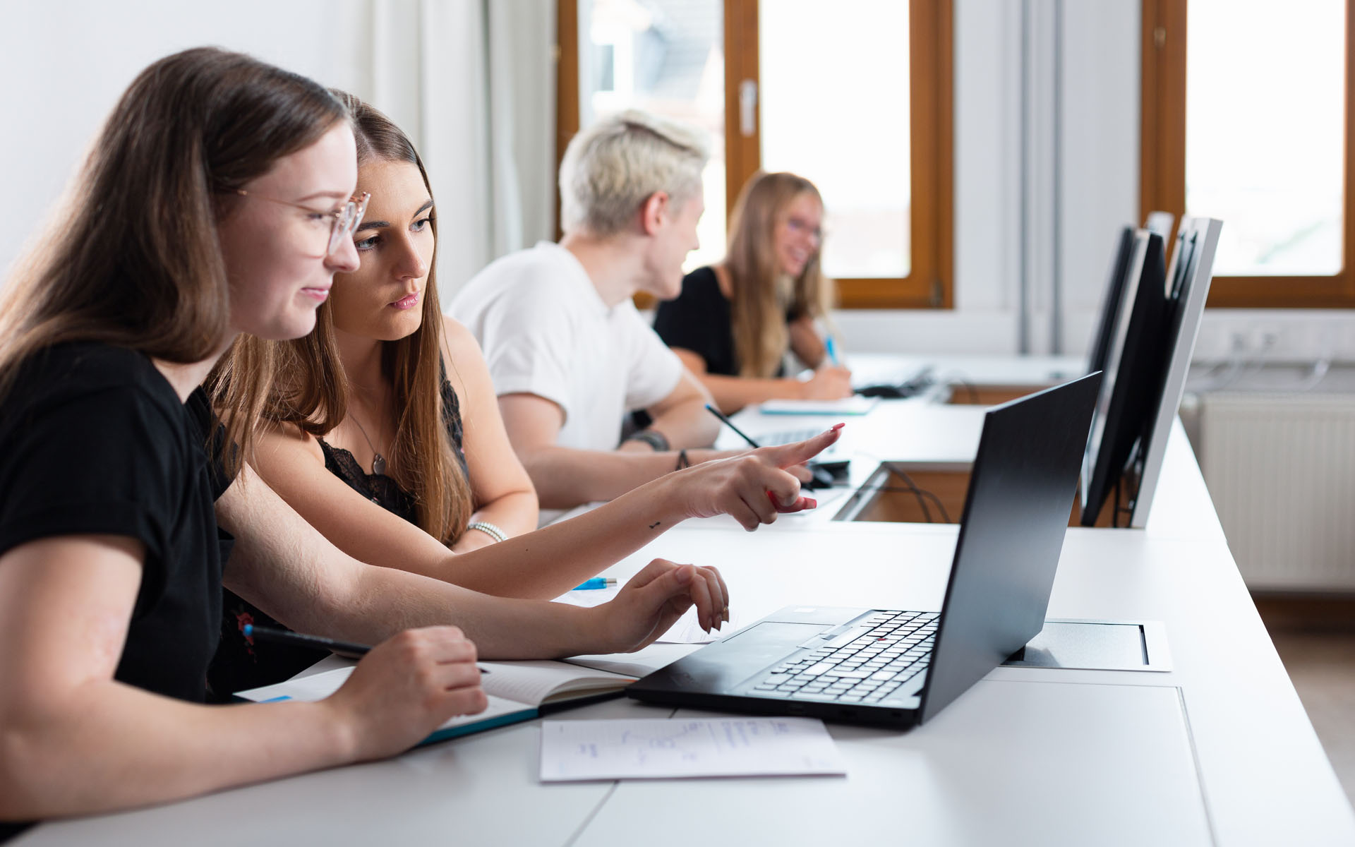 Vier Studierende mit Laptops in Seminarraum von der Seite