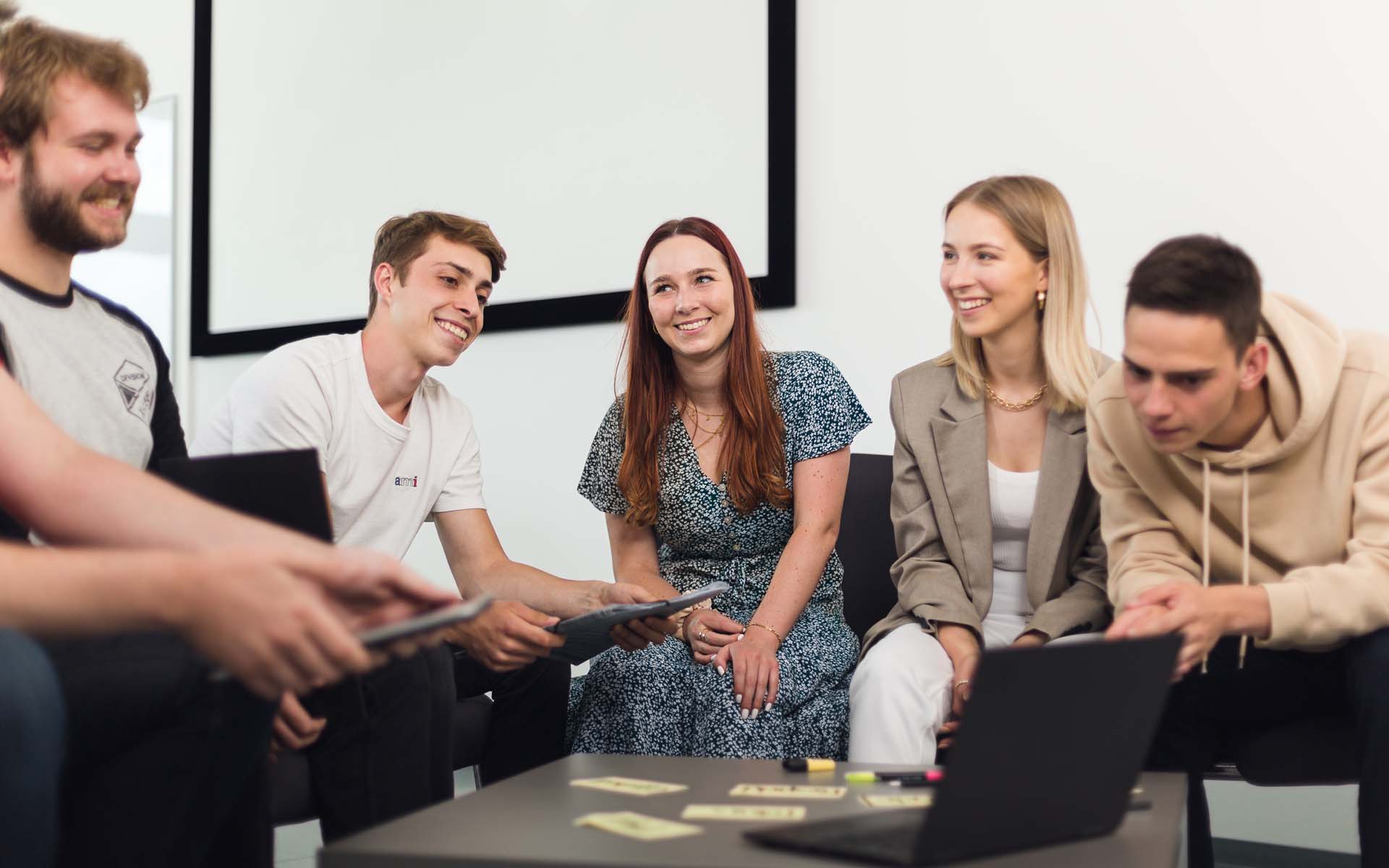 Studierende des Studiengangs SD sitzen mit Laptops und tablets in einem Kreis.