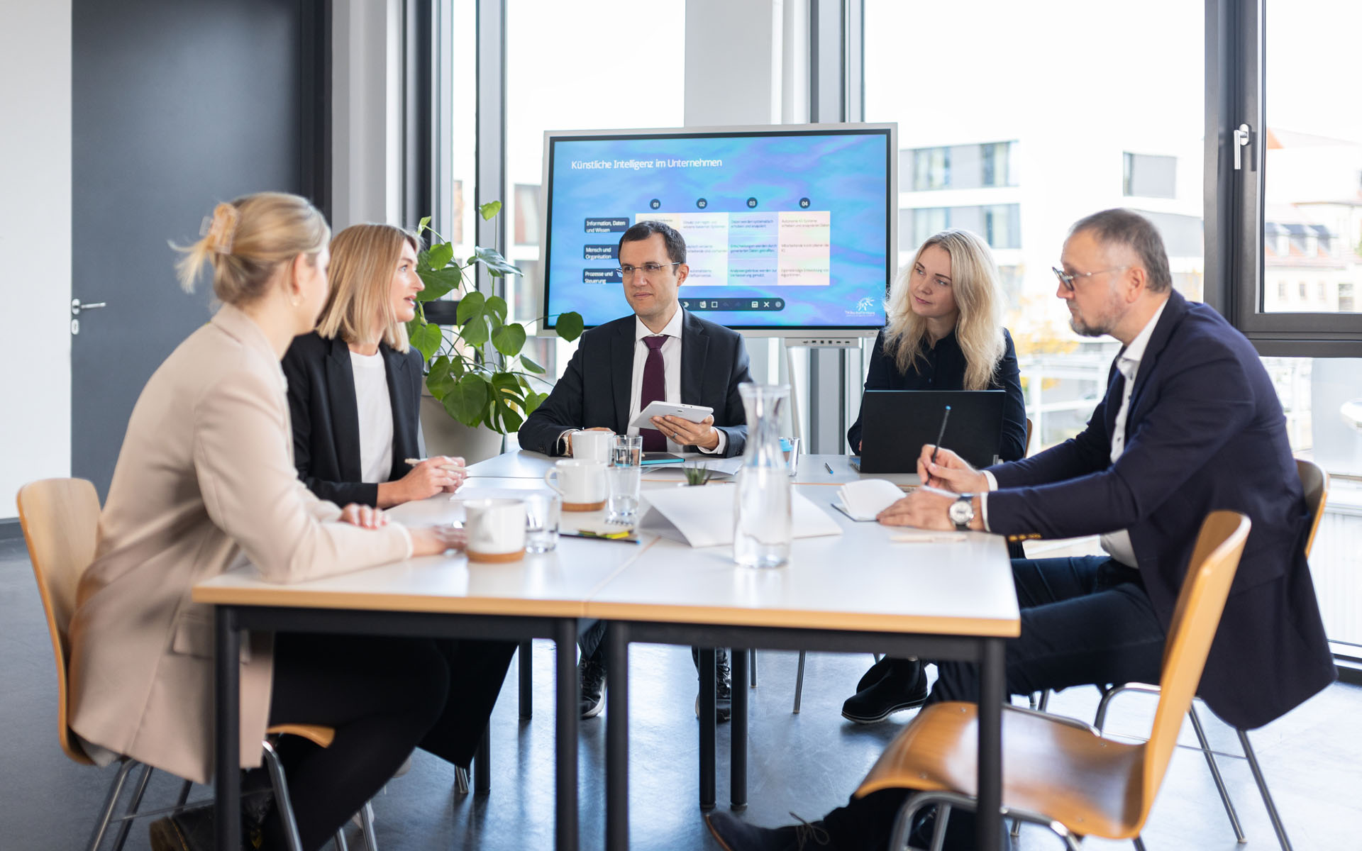 Fünf Personen sitzen an einem Meeting-Tisch 