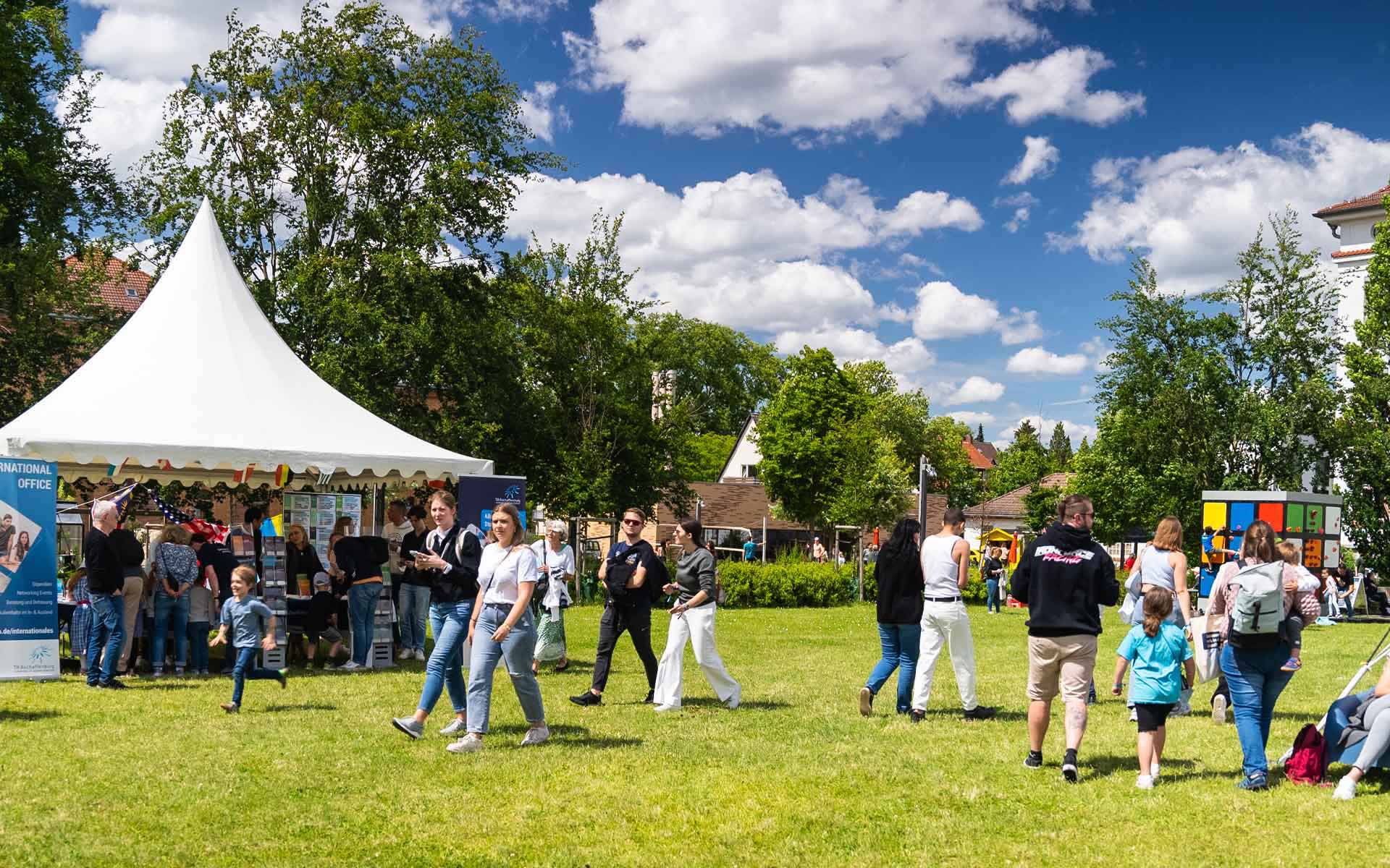 Besucherinnen und Besucher laufen über die Campuswiese zwischen verschiedenen Ständen vor strahlend blauem Himmel