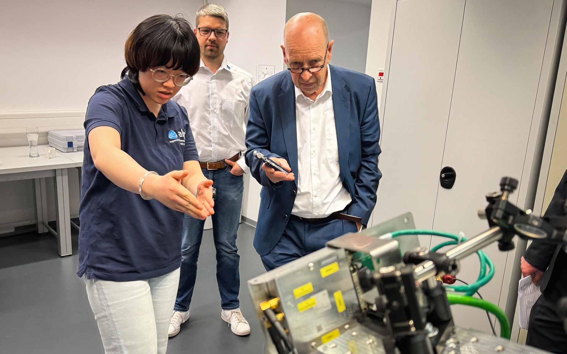 Labormitarbeiterin erklärt dem Gutachter die Arbeit der Forschungsgruppe hinsichtlich der Laser-Lichtführung entlang des Industrie-Roboters