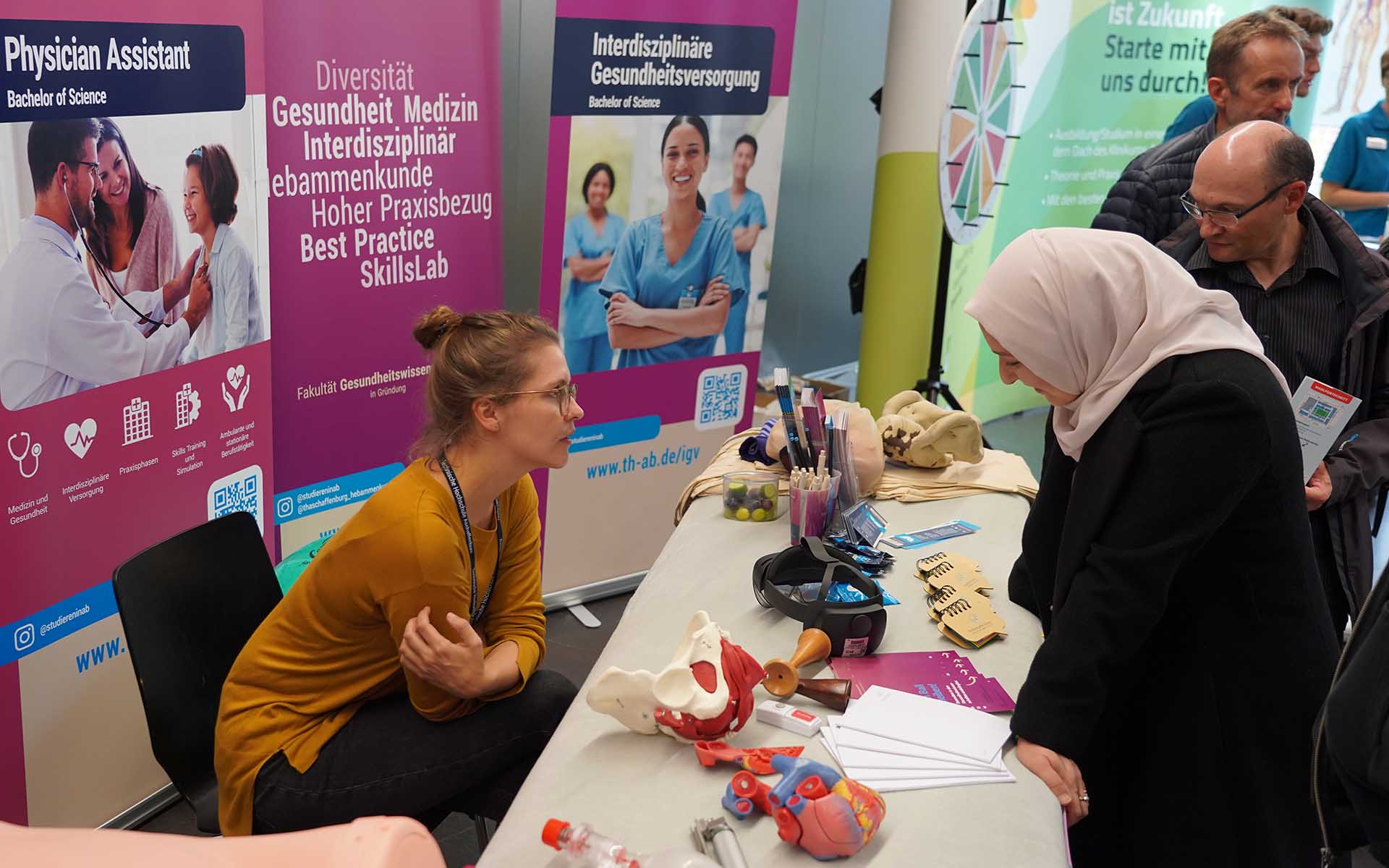 Eine Frau mit Kopftuch informiert sich am Stand der Fakultät Gesundheit 