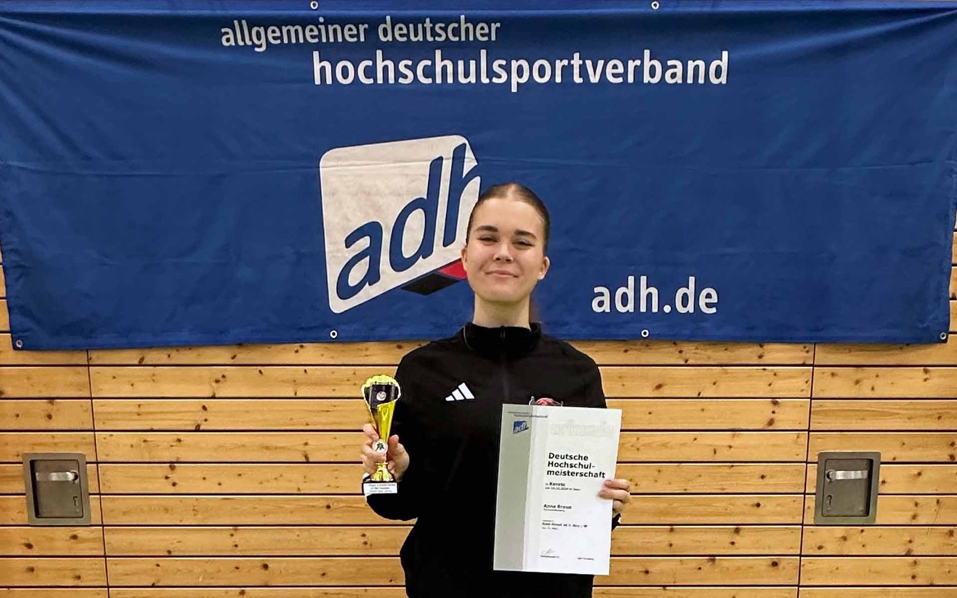 Siegerin Anna Braun mit Urkunde und Pokal in der Hand vor Hochschulverbandsbanner