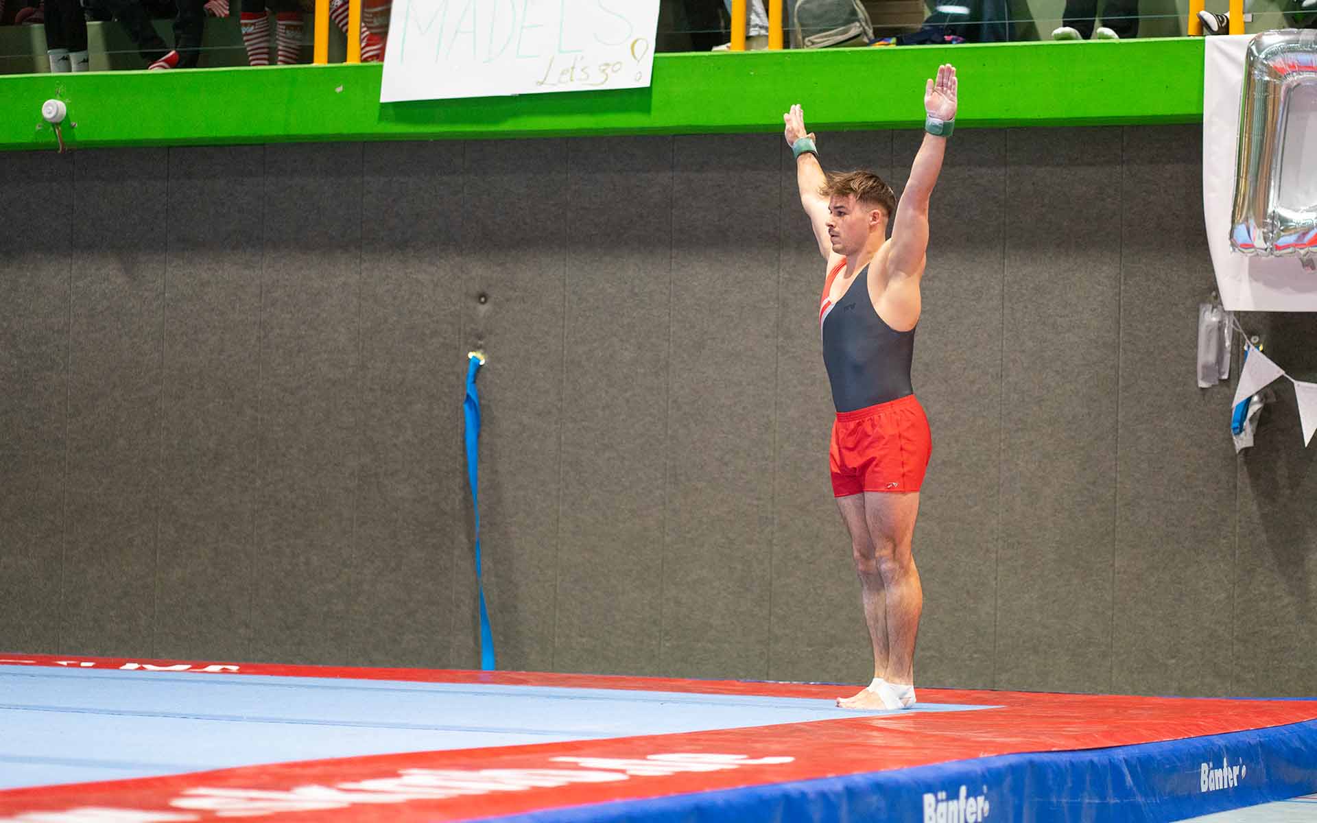 Maximilian in Startposition mit ausgestreckten Armen auf der Matte vor der Tribüne