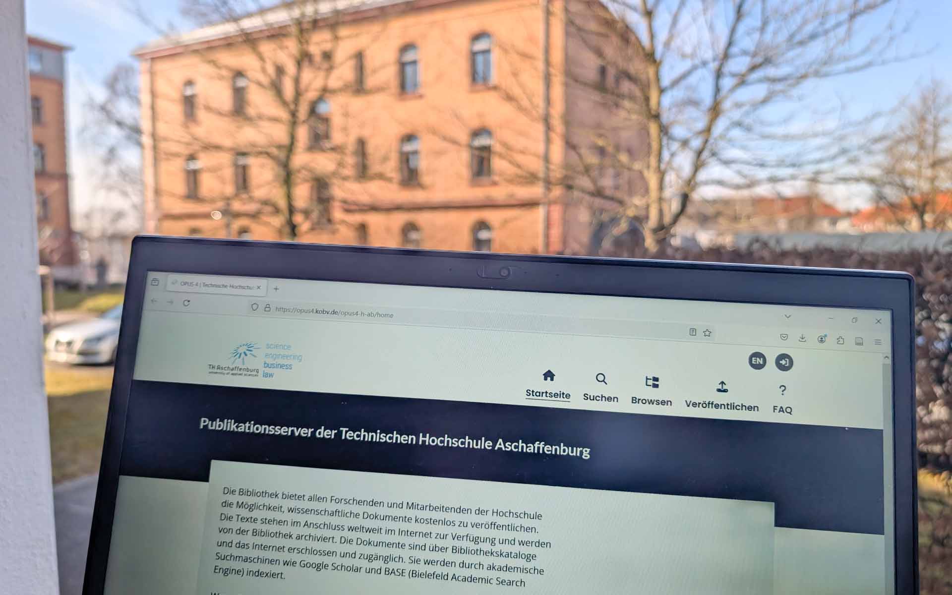 Bildschirm mit Website zum Publikationsserver vor Fenster mit rotem Backsteingebäude der TH