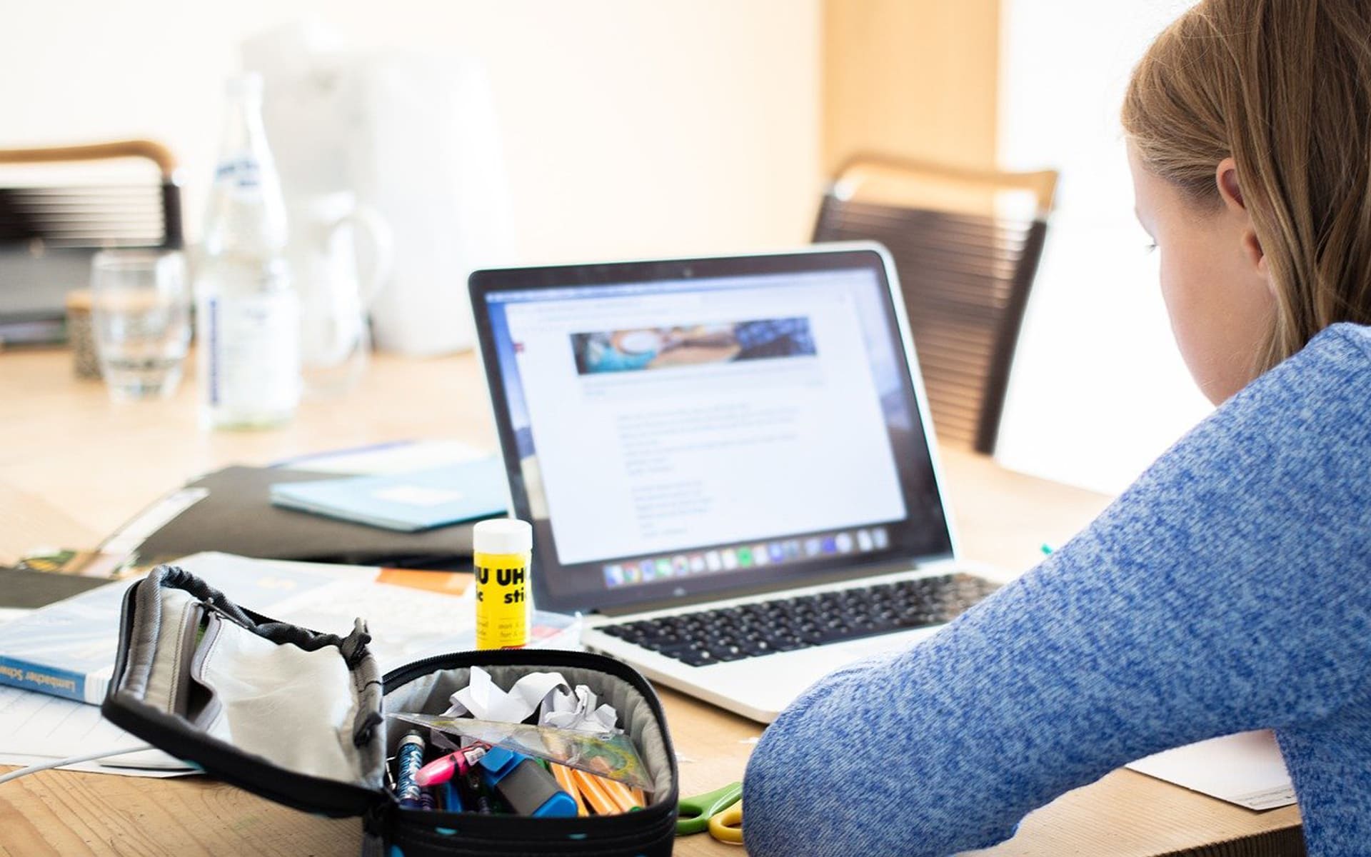 Schülerin arbeitet mit Mäppchen und Laptop an einem Tisch