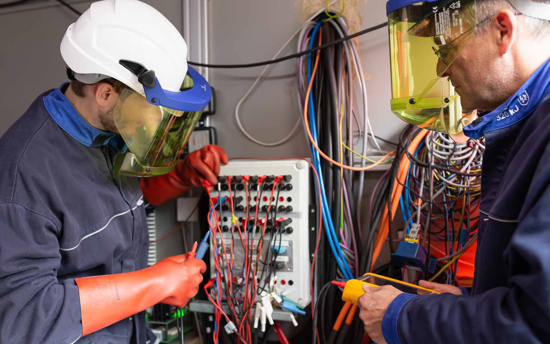 Zwei Männer in Schutzkleidung arbeiten an der Elektrik.