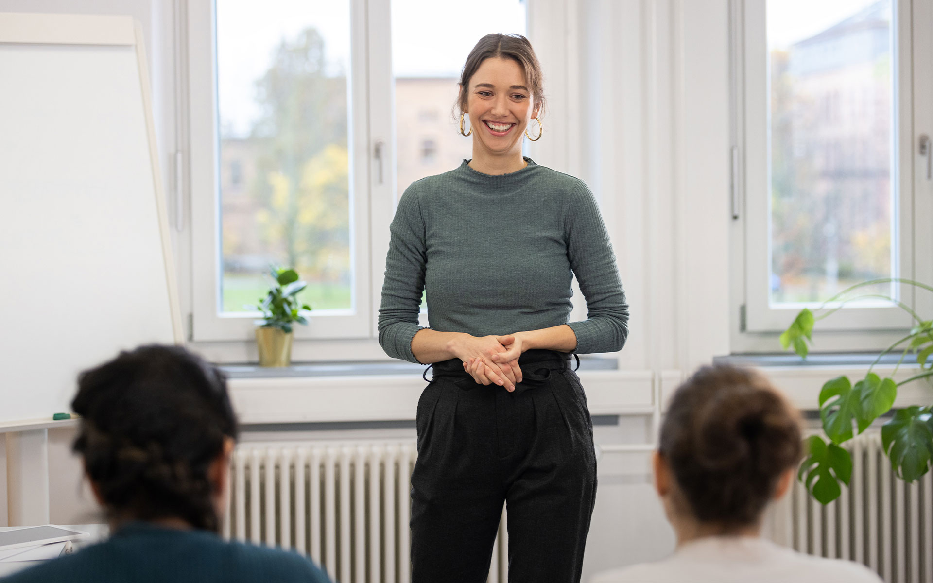 Eine junge Professorin steht zwei Personen bei einem Vortrag mit einem Lachen gegenüber. 