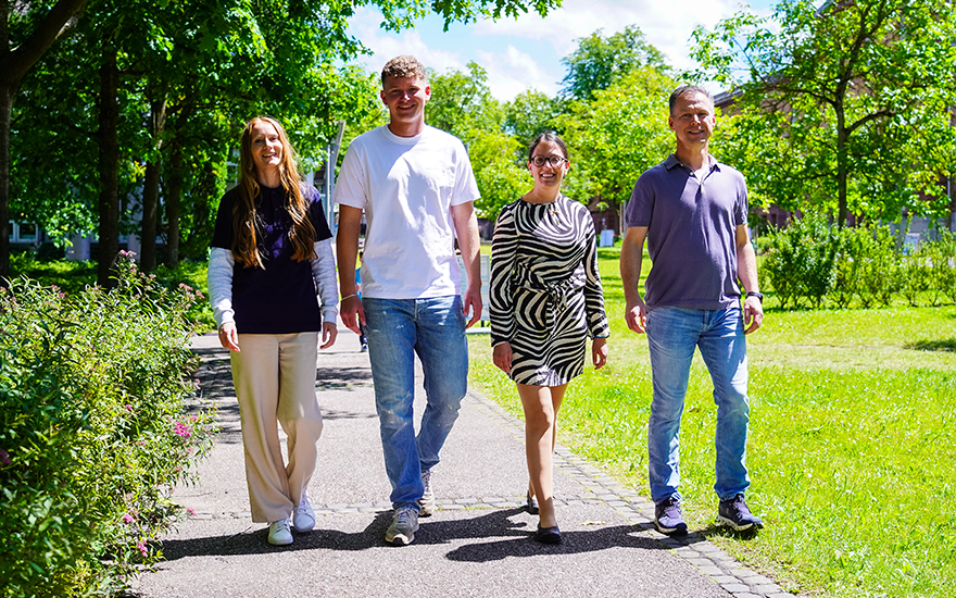 vier Angestellte der TH Aschaffenburg laufen nebeneinander über den Campus.